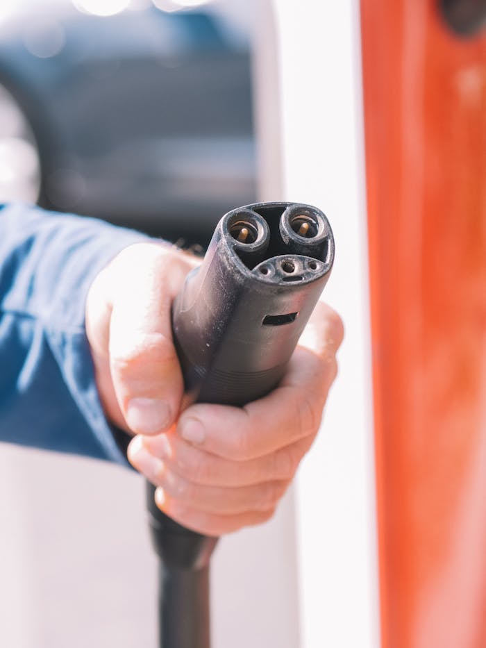 Close-up of a person holding an electric car charging plug, representing renewable energy use.